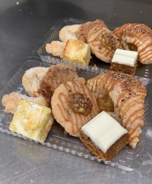 Two trays of assorted pastries, including cookies, bars, and flaky treats, drizzled with icing and topped with nuts.