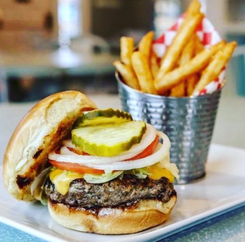 A juicy cheeseburger with lettuce, tomato, pickles, and onions, served with a side of crispy French fries.