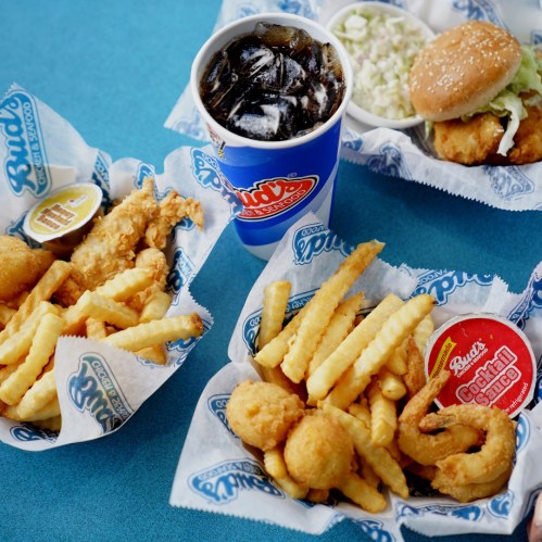 A colorful spread of fried seafood, crinkle-cut fries, a burger, coleslaw, and a drink on a blue table.