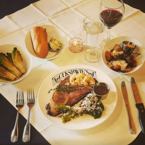 A beautifully arranged dinner table featuring a plate of beef, sides, bread, and drinks, set with elegant utensils.