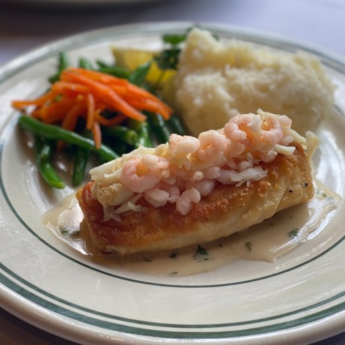 A plate featuring a fish fillet topped with shrimp, served with green beans, carrots, and mashed potatoes.