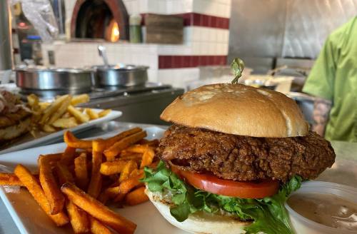 A crispy fried chicken sandwich with lettuce and tomato, served with sweet potato fries on the side.