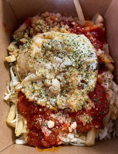A box of fries topped with marinara sauce, a fried egg, herbs, and grated cheese.