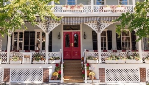 Charming restaurant exterior with a pink door, white trim, and flower-filled planters on a sunny day.