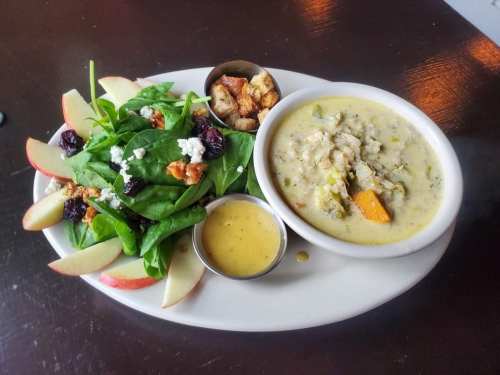 A plate with a spinach salad, apple slices, and a bowl of creamy soup with vegetables and grains.
