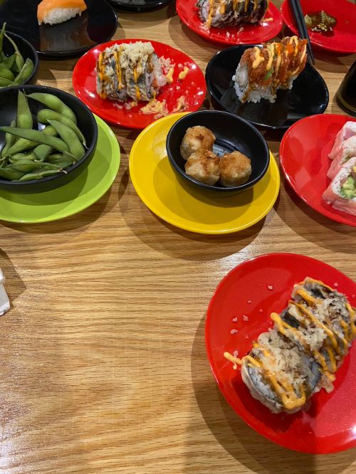 A table with colorful plates featuring sushi, edamame, and dumplings, showcasing a variety of Japanese dishes.