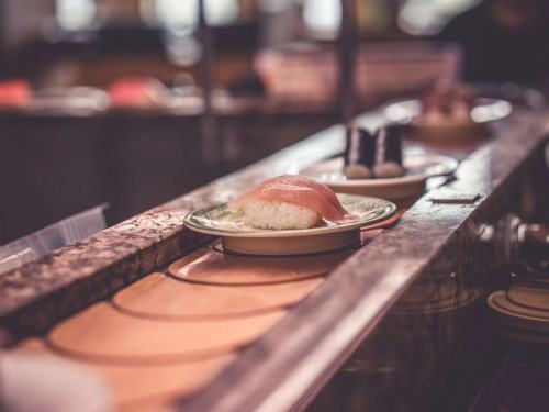 A plate of sushi with a slice of fish on top, placed on a conveyor belt in a sushi restaurant.