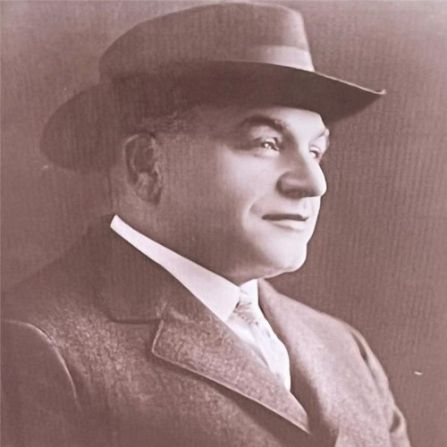 A sepia-toned portrait of a man in a suit and hat, looking confidently to the side.