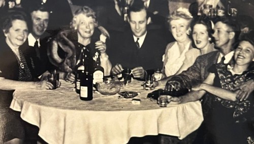 A group of eight people seated around a table, enjoying drinks and conversation in a vintage setting.