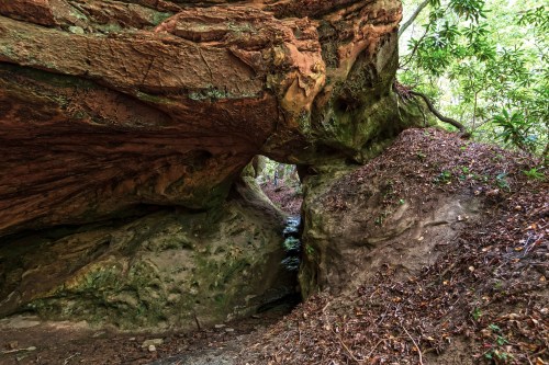 A rocky landscape featuring a large overhanging rock formation and a small stream flowing through a narrow passage.