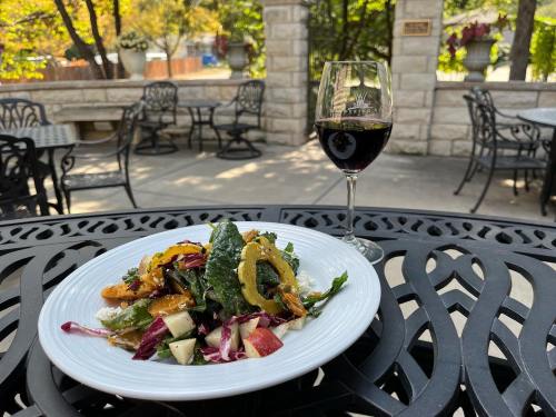 A fresh salad with greens, apples, and roasted squash, paired with a glass of red wine on a patio table.