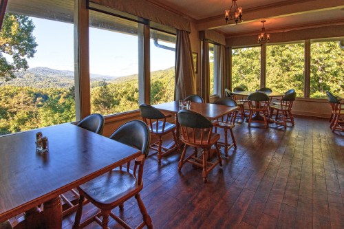 A cozy dining area with wooden tables and chairs, featuring large windows that offer a scenic view of the outdoors.