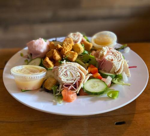 A plate of salad with mixed greens, sliced turkey and ham, cucumbers, tomatoes, and croutons, served with dressing.