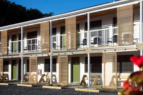 A modern motel exterior with wooden slats, balconies, and green doors under a clear blue sky.
