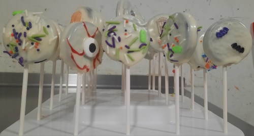 A display of decorated cake pops with colorful sprinkles and designs, arranged on sticks.