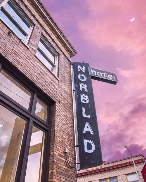 Sign for Norblad Hotel on a brick building against a colorful sunset sky.
