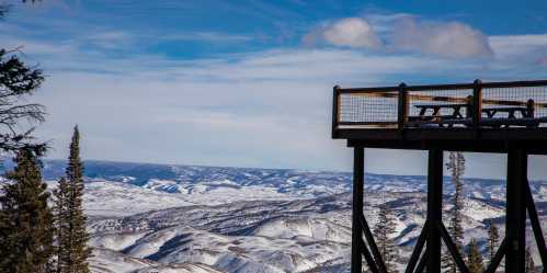 A snowy mountain landscape with a viewing platform overlooking rolling hills and a blue sky.