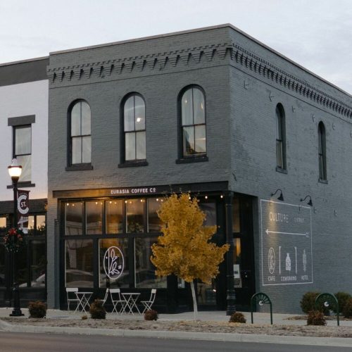 A modern coffee shop with large windows, a yellow tree in front, and a sign displaying "Eurasia Coffee Co." on the side.