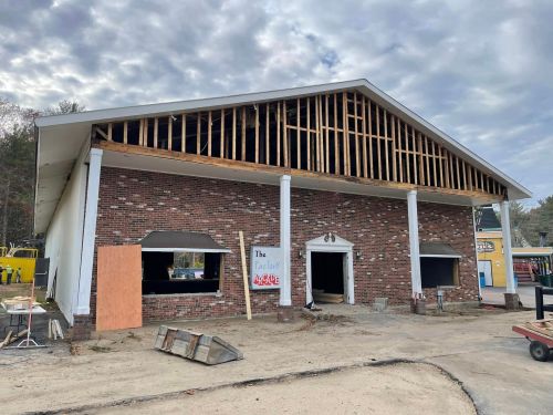 A partially constructed building with exposed framing, brick facade, and boarded windows under a cloudy sky.