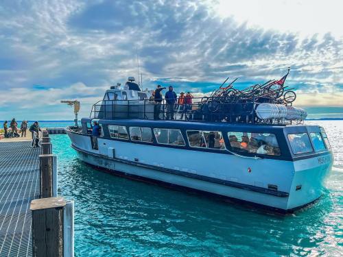 A boat docked at a pier with passengers on board, surrounded by calm blue waters and a cloudy sky.