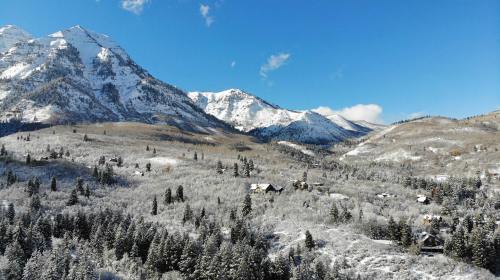 Snow-covered mountains and trees under a clear blue sky, with a few houses nestled in the valley below.