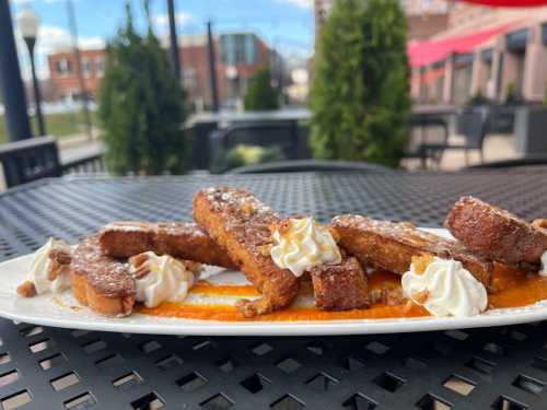 A plate of French toast sticks drizzled with sauce, topped with whipped cream and nuts, on a table outdoors.