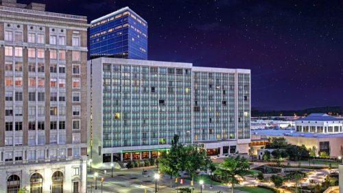 Cityscape at night featuring a modern hotel, historic buildings, and a starry sky.