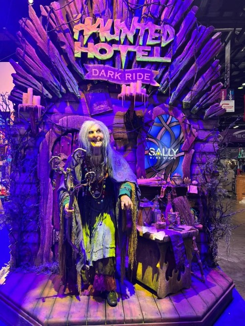A spooky witch figure stands in front of a haunted hotel display, surrounded by eerie decorations and dim lighting.
