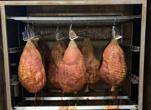 Hanging cured hams in a meat curing chamber, showcasing their rich, golden-brown color.