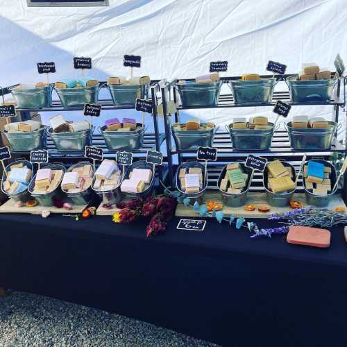 A display of colorful handmade soaps in baskets, with labels, set up on a table under a white tent.