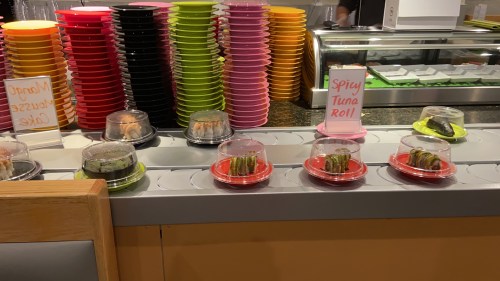 A sushi display with colorful plates and a sign for "Spicy Tuna Roll" in a restaurant setting.