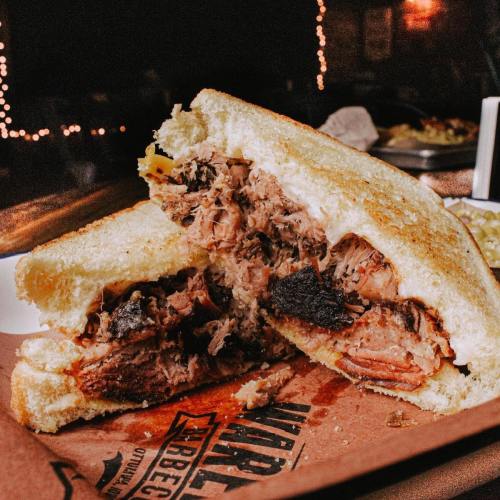 A close-up of a hearty sandwich filled with pulled pork, served on toasted bread with a smoky appearance.