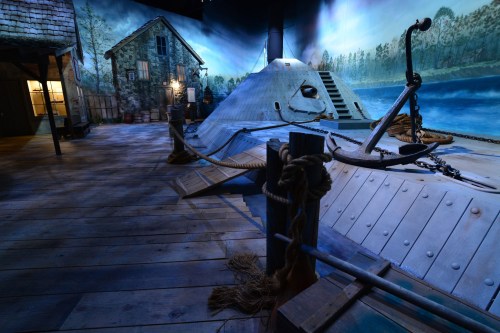 A vintage submarine displayed in a scenic maritime setting with a painted backdrop of trees and water.