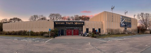 Exterior view of the Whydah Pirate Museum, featuring a large sign and a parking lot at dusk.