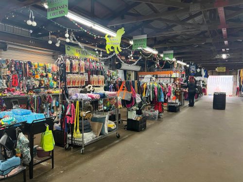 A pet shop interior with colorful merchandise displays, including collars, harnesses, and pet clothing, in a market setting.