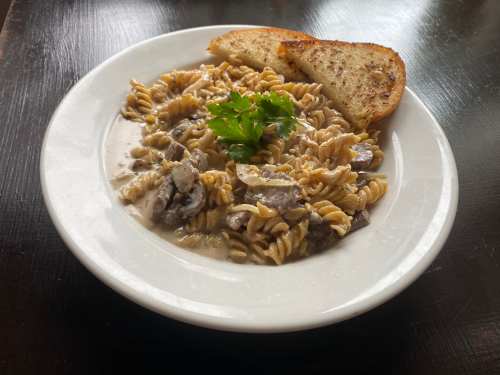 A plate of creamy pasta with mushrooms, garnished with parsley, served with a slice of toasted bread.