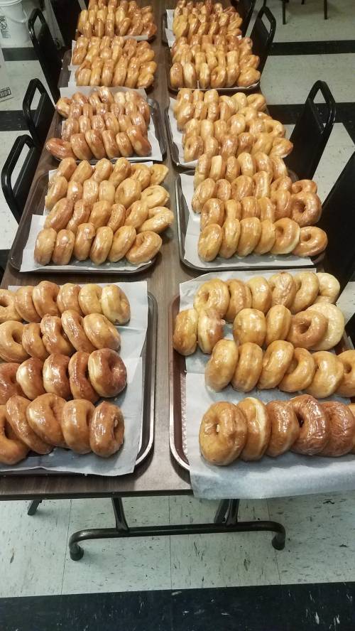 A table filled with trays of freshly glazed donuts arranged in neat rows.