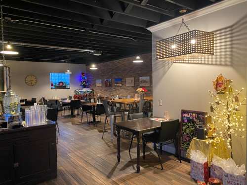 Cozy restaurant interior with wooden floors, tables, festive decorations, and warm lighting.