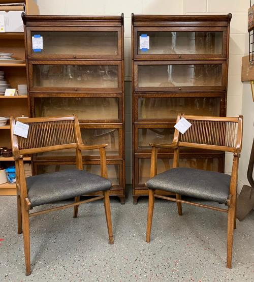 Two wooden display cabinets with glass doors and two matching chairs in a thrift store setting.