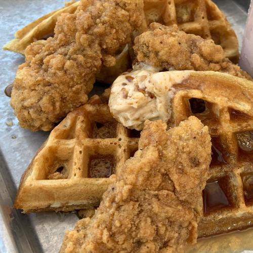 A close-up of crispy fried chicken pieces on golden waffles, drizzled with syrup and a dollop of butter.
