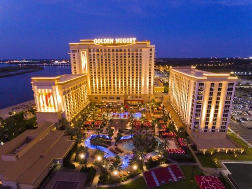 Aerial view of the Golden Nugget hotel, illuminated at night, with a pool and palm trees in the foreground.