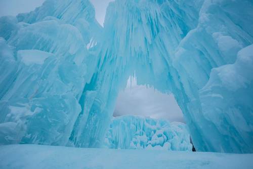 A stunning ice formation with towering blue icicles creating a natural archway in a winter landscape.