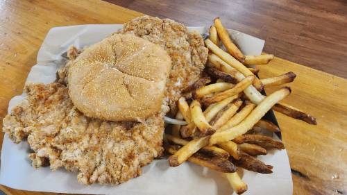 A plate with two fried chicken fillets, a bun, and a serving of crispy French fries on a wooden table.