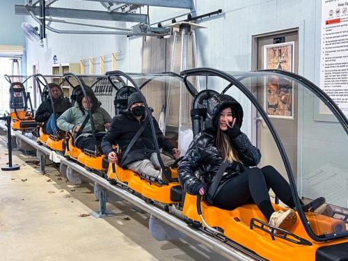 A group of five people seated in a ride, wearing winter clothing and safety harnesses, ready for an adventure.