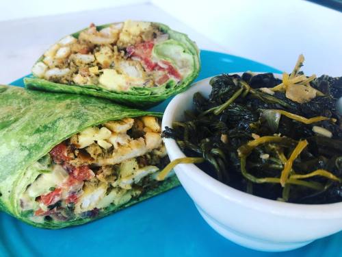A green spinach wrap filled with eggs, tomatoes, and spices, served with a side of sautéed greens in a white bowl.