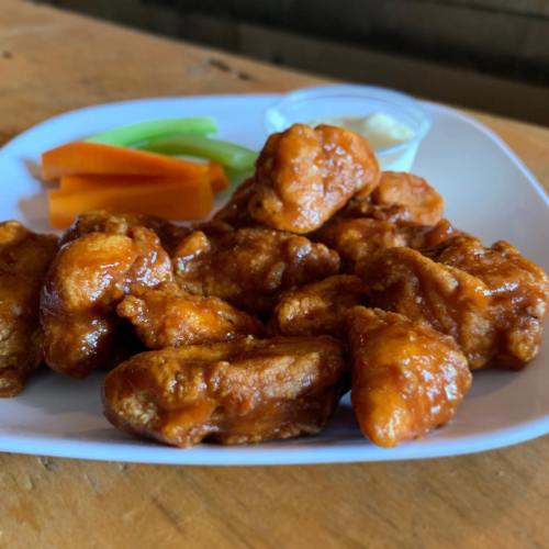A plate of saucy chicken wings with celery and carrot sticks, accompanied by a small cup of dipping sauce.