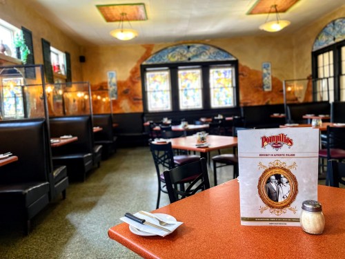 A cozy restaurant interior with stained glass windows, booths, and a menu on a table.