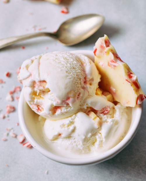 A bowl of creamy ice cream with peppermint pieces, topped with a white chocolate bark and scattered peppermint bits.