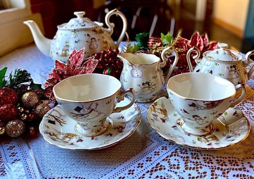 A festive tea set with snowman designs, surrounded by holiday decorations and a lace tablecloth.
