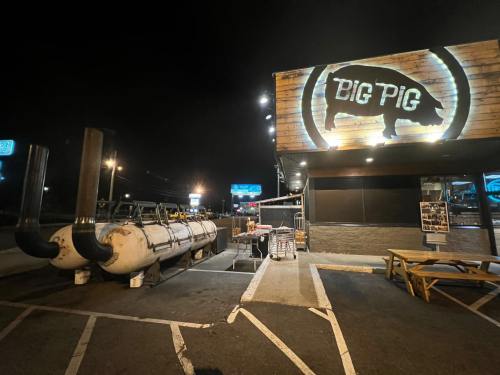 Exterior view of Big Pig restaurant at night, featuring a large smoker and illuminated sign with a pig logo.